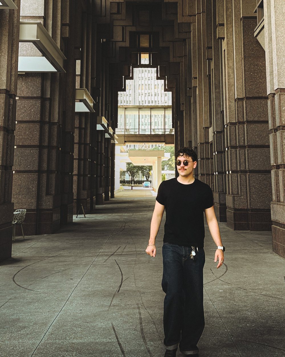 Garrett Grainger walking through a granite colonnade in a black t-shirt and sunglasses